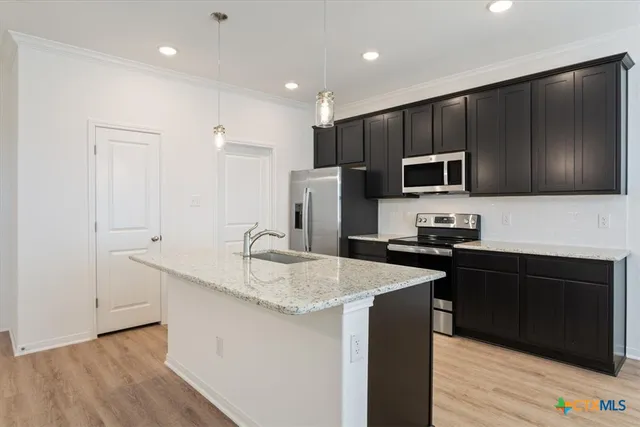 a kitchen with kitchen island granite countertop stainless steel appliances a sink a stove a refrigerator cabinets and wooden floor