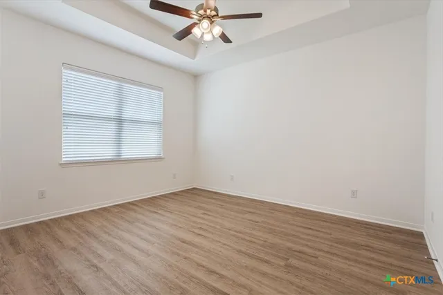an empty room with wooden floor chandelier fan and windows