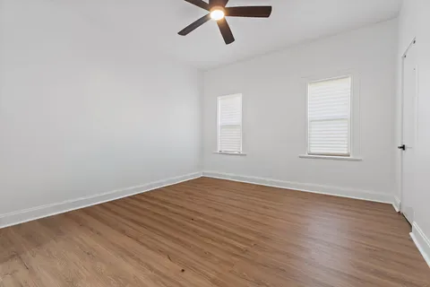 an empty room with wooden floor chandelier fan and windows