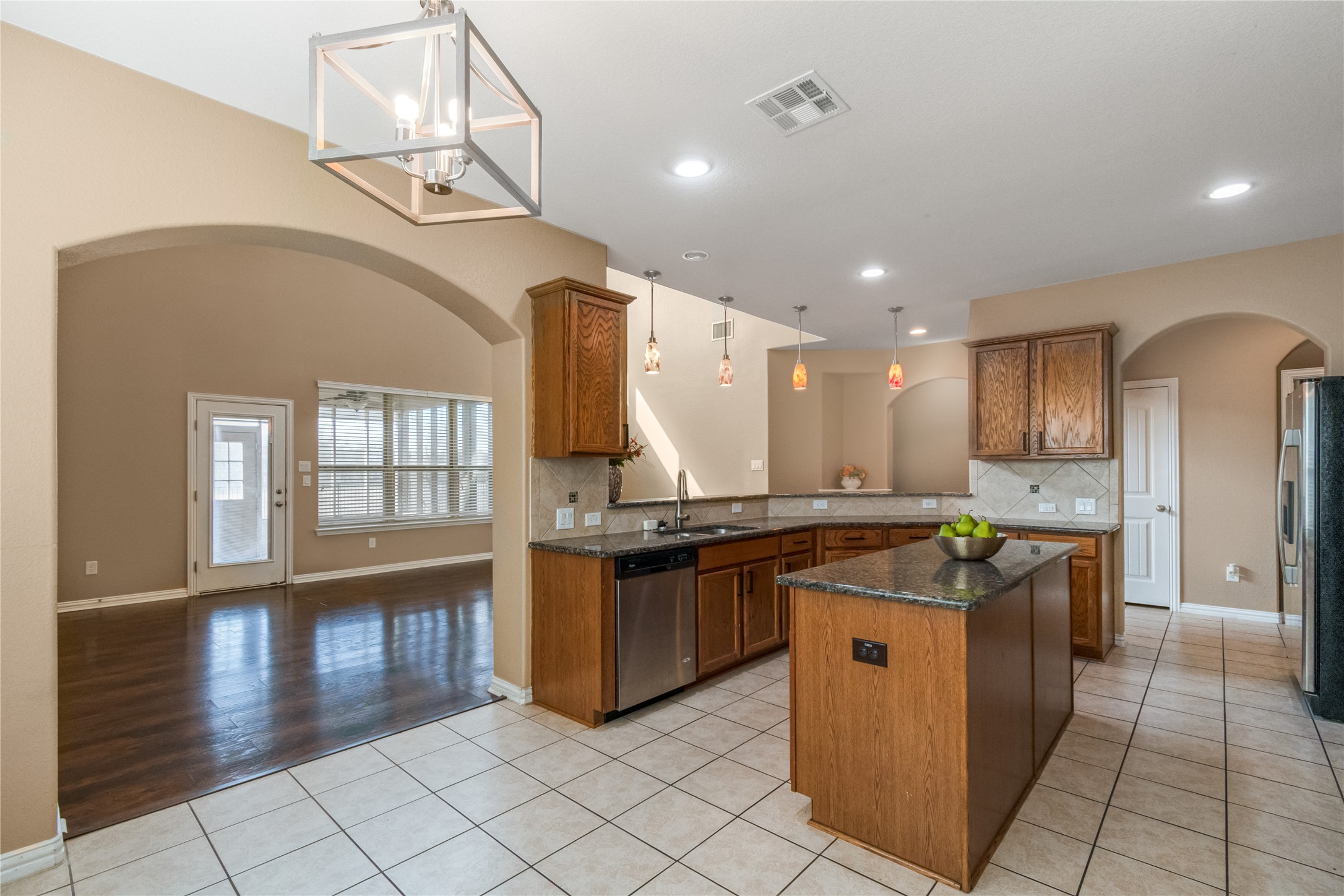 3413 Grail Hollows Road Pflugerville, TX 78660 - Photo 7 of 36 Kitchen with arched walkways, light tile patterned flooring, wood finish cabinets, a center island, and dark stone counters