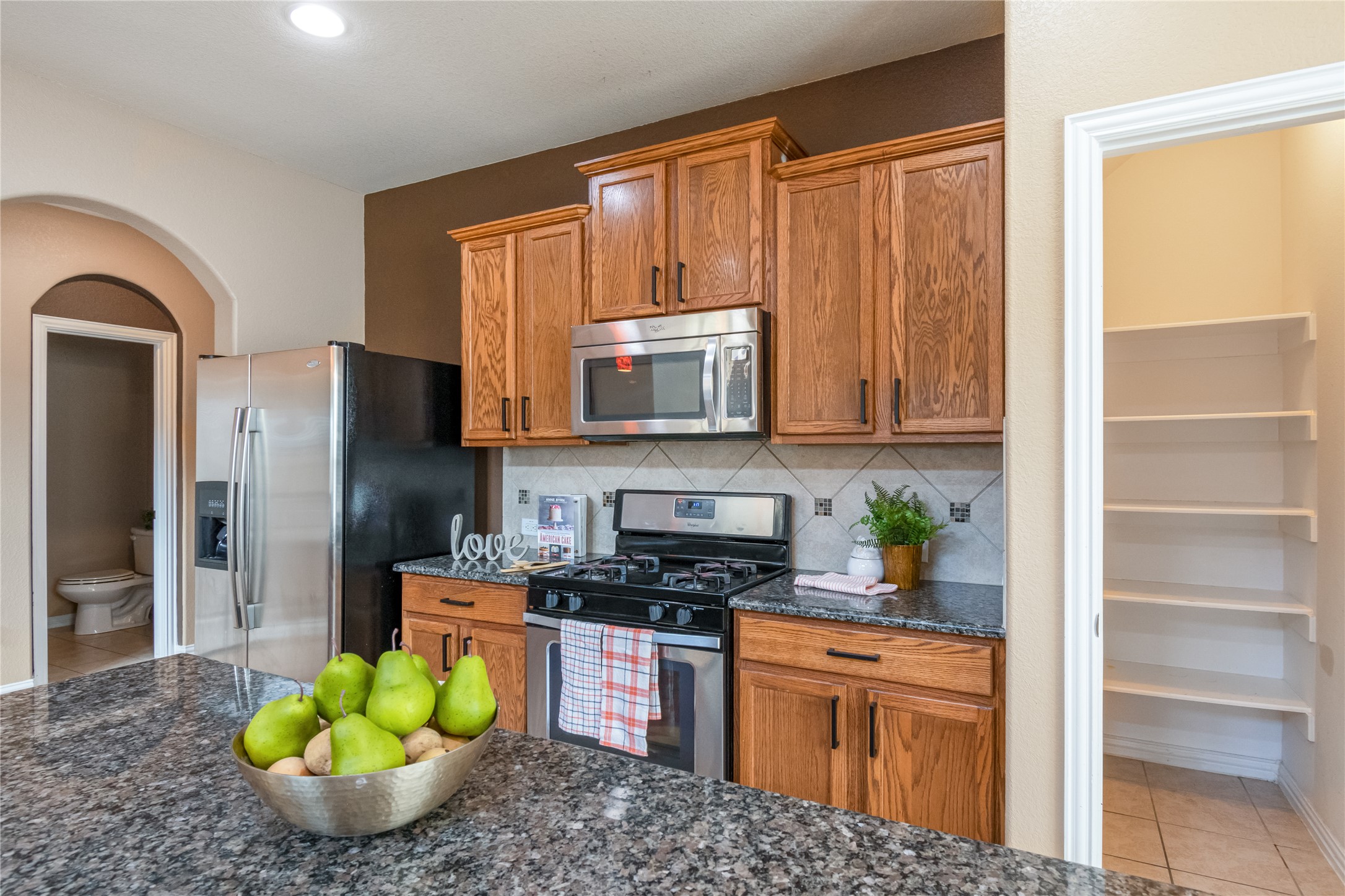 3413 Grail Hollows Road Pflugerville, TX 78660 - Photo 10 of 36 Kitchen featuring stainless steel appliances, dark stone countertops, wood finish cabinetry, and light tile patterned floors