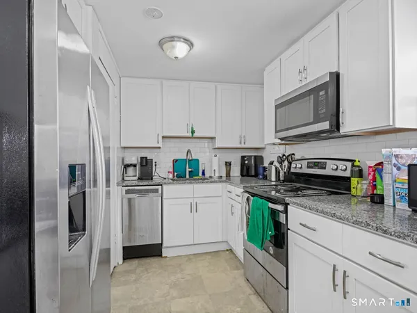 a kitchen with stainless steel appliances granite countertop a refrigerator sink stove and white cabinets