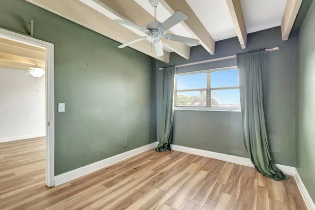 an empty room with wooden floor fan and windows