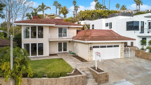 a view of a white house with large windows and a yard with plants and palm trees