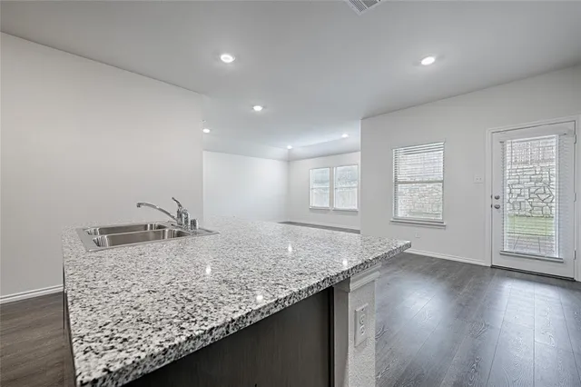an empty room with wooden floor and a kitchen