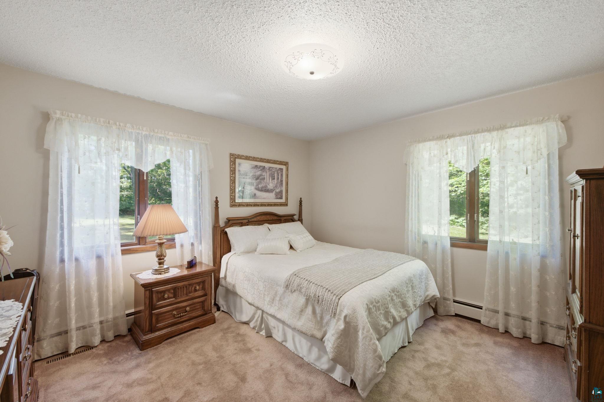 27485 South Kane Road Ashland, WI 54806 - Photo 13 of 35 Bedroom featuring plush carpeting, two windows with white sheer curtains, a textured ceiling, and a flush-mount ceiling light fixture