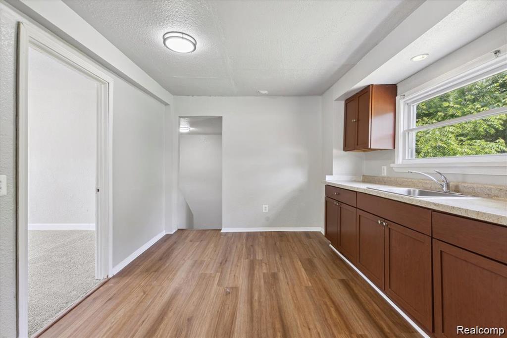 3140 Moore Street Inkster, MI 48141 - Photo 5 of 18 Kitchen area featuring wood-finish flooring, ample brown cabinetry, and a window above the sink
