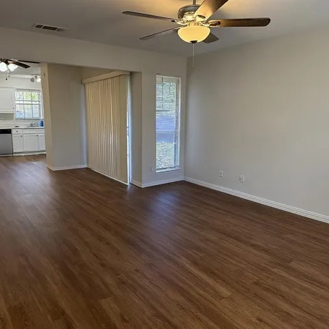 an empty room with wooden floor fan and windows