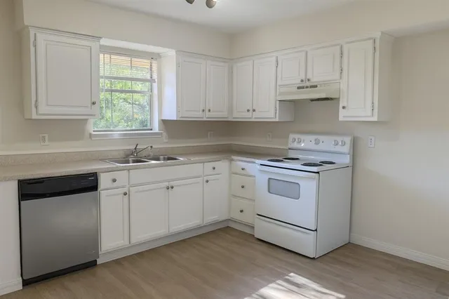 a kitchen with white cabinets appliances and a window