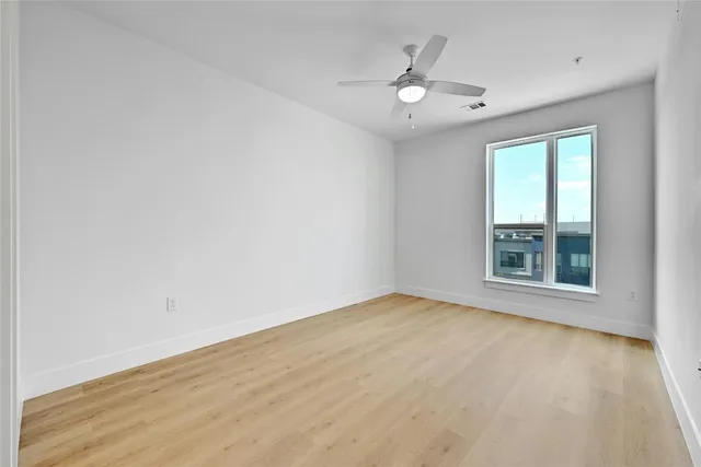 an empty room with wooden floor chandelier fan and windows