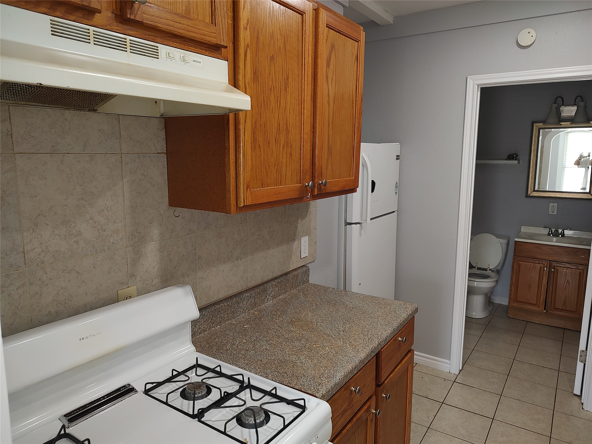 2617 Wheless Lane Austin, TX 78723 - Photo 11 of 14 Kitchen featuring white appliances, wood finish cabinetry, light tile patterned floors, decorative backsplash, and dark countertops