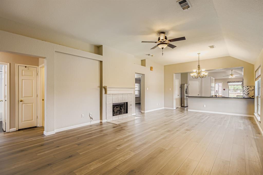 5452 Buckskin Drive The Colony, TX 75056 - Photo 10 of 31 Unfurnished living room featuring ceiling fan, a chandelier, a tile fireplace, light wood-style floors, and vaulted ceiling
