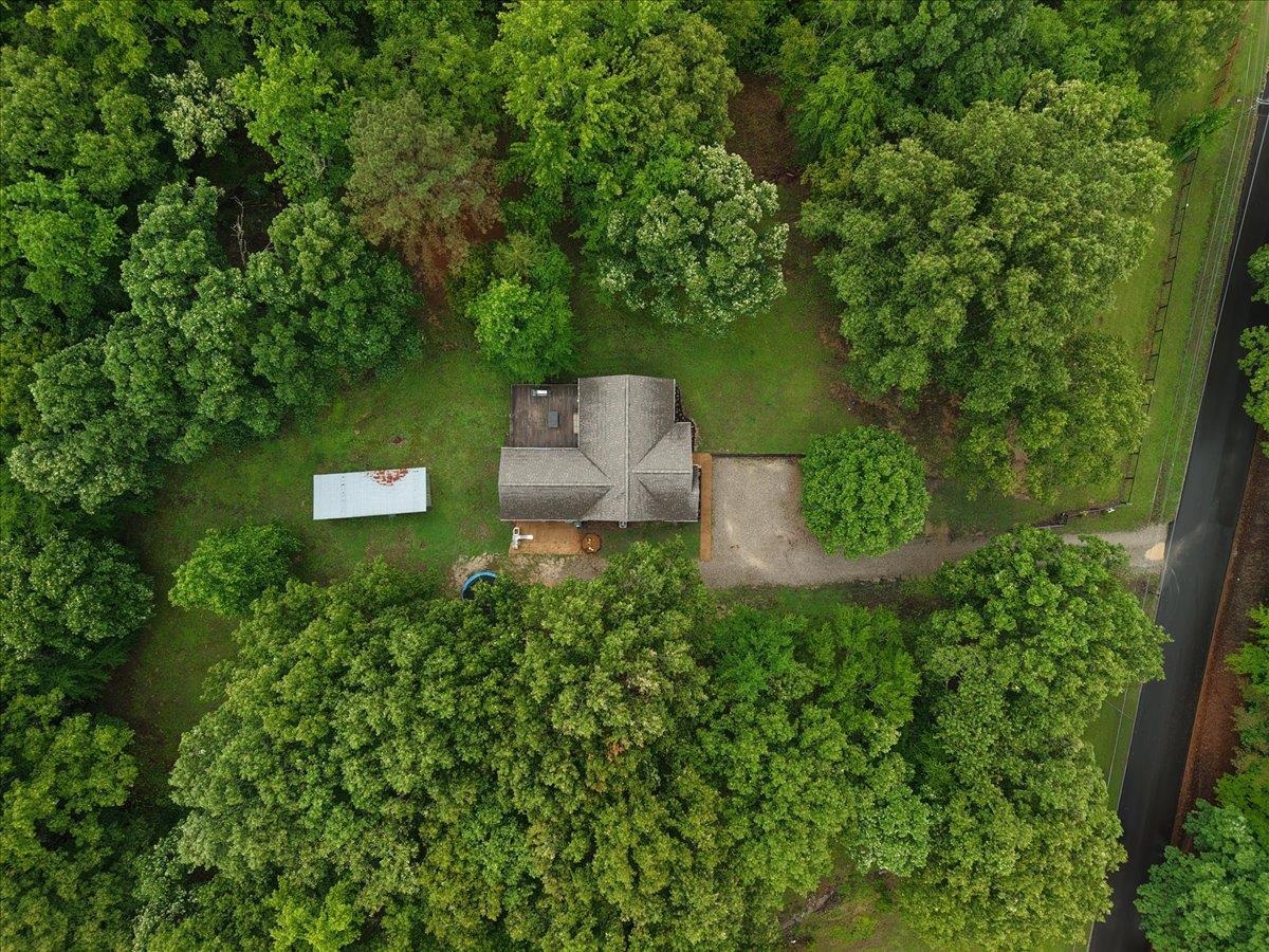 150 Liberty Road Moscow, TN 38057 - Photo 34 of 36 Aerial perspective of a single-story residence surrounded by mature trees, featuring a gravel driveway, a detached storage building, and a fenced perimeter