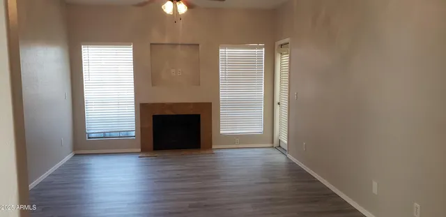an empty room with wooden floor fireplace and windows