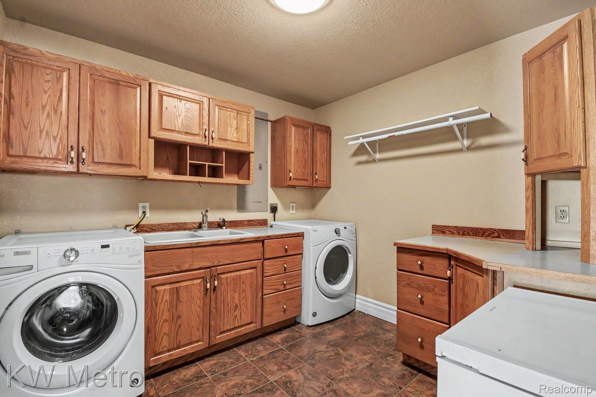 2682 East Haskell Lake Road Harrison, MI 48625 - Photo 18 of 61 Utility room featuring wood-finish cabinetry, a double sink, ample counter space, and durable tile flooring
