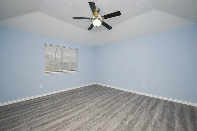 an empty room with wooden floor ceiling fan and windows