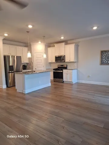 a kitchen with stainless steel appliances kitchen island granite countertop a stove and a wooden floors