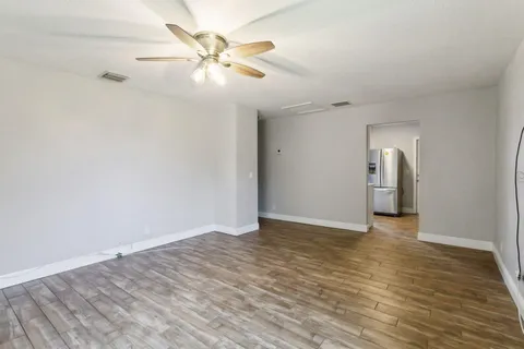 a view of an empty room with wooden floor and a ceiling fan