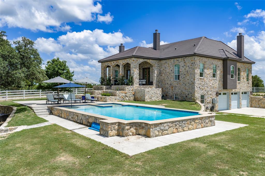 501 Upper Denton Road Weatherford, TX 76085 - Photo 27 of 40 Stone exterior residence featuring a tiled roof, multi-car garage, tiered outdoor living spaces, a rectangular swimming pool, and white fencing