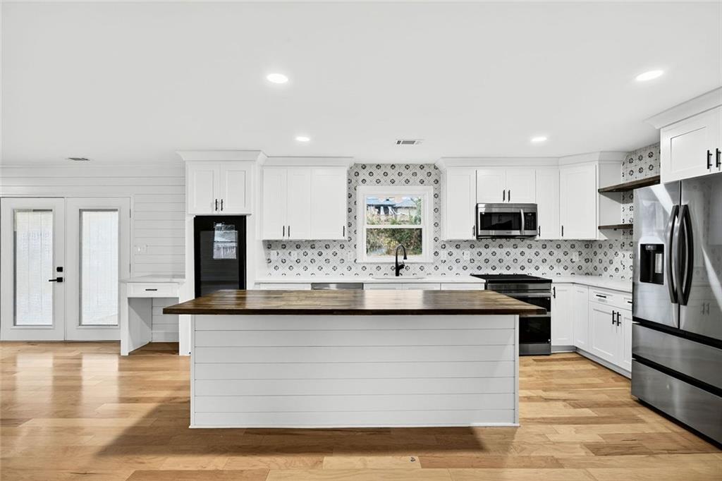 3365 Ardley Road Southwest Atlanta, GA 30311 - Photo 9 of 34 a large white kitchen with stainless steel appliances kitchen island granite countertop a stove a sink a refrigerator and white cabinets with wooden floor