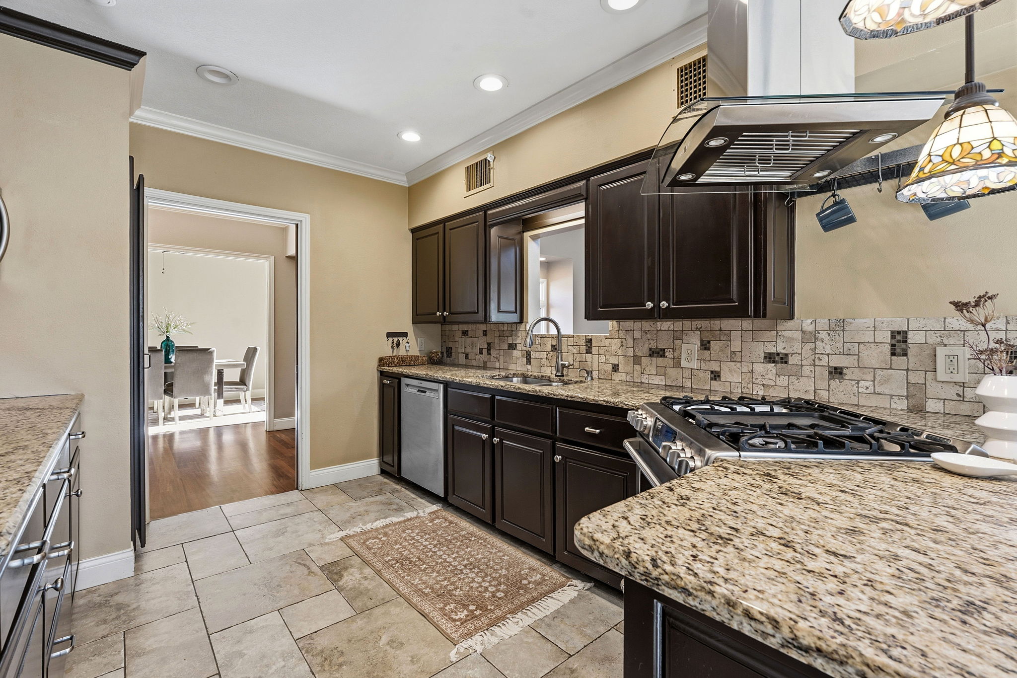 4601 Creek Ridge Austin, TX 78735 - Photo 12 of 40 Kitchen featuring light stone counters, exhaust hood, ornamental molding, stainless steel appliances, and dark wood finish cabinetry