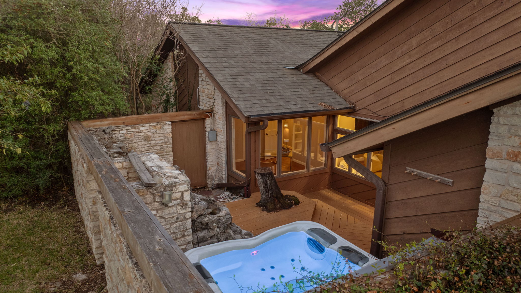 4601 Creek Ridge Austin, TX 78735 - Photo 35 of 40 Property exterior at dusk featuring stone siding, a hot tub, a wooden deck, and a shingled roof