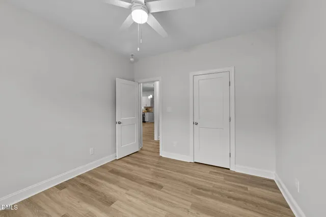 a view of an empty room with wooden floor fan and window