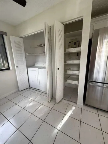 a view of a refrigerator in kitchen and an empty room in wooden floor