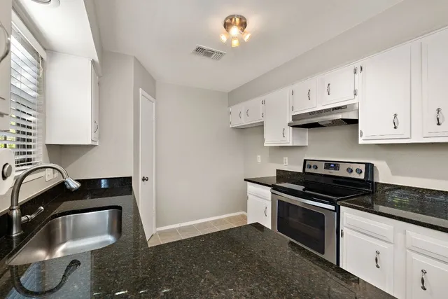 a kitchen with granite countertop a sink a stove and cabinets