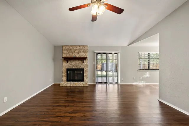 an empty room with wooden floor fireplace and windows