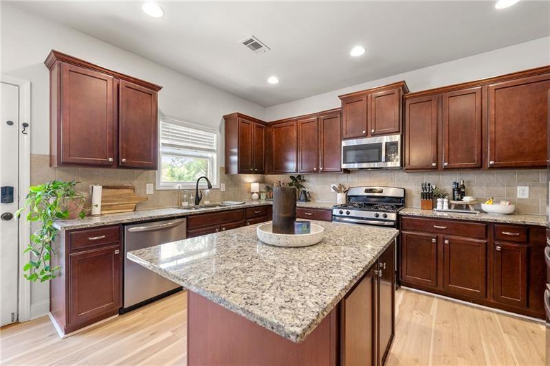 4970 Creekside Lane Powder Springs, GA 30127 - Photo 13 of 45 a kitchen with kitchen island granite countertop wooden cabinets a stove top oven a sink and dishwasher with wooden floor