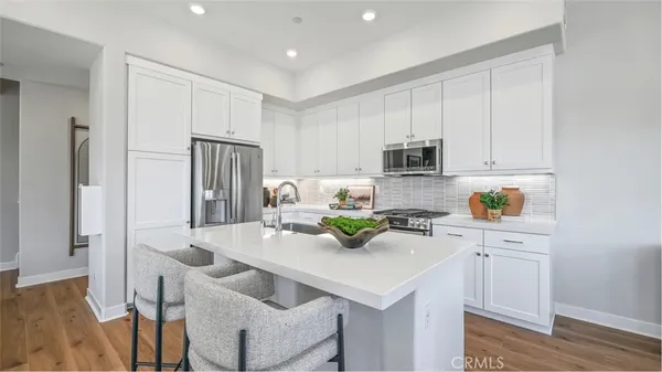 a kitchen with stainless steel appliances granite countertop a refrigerator a sink a stove and white cabinets with wooden floor