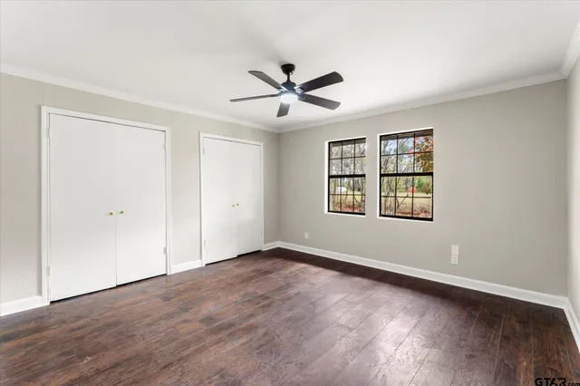 an empty room with wooden floor ceiling fan and windows
