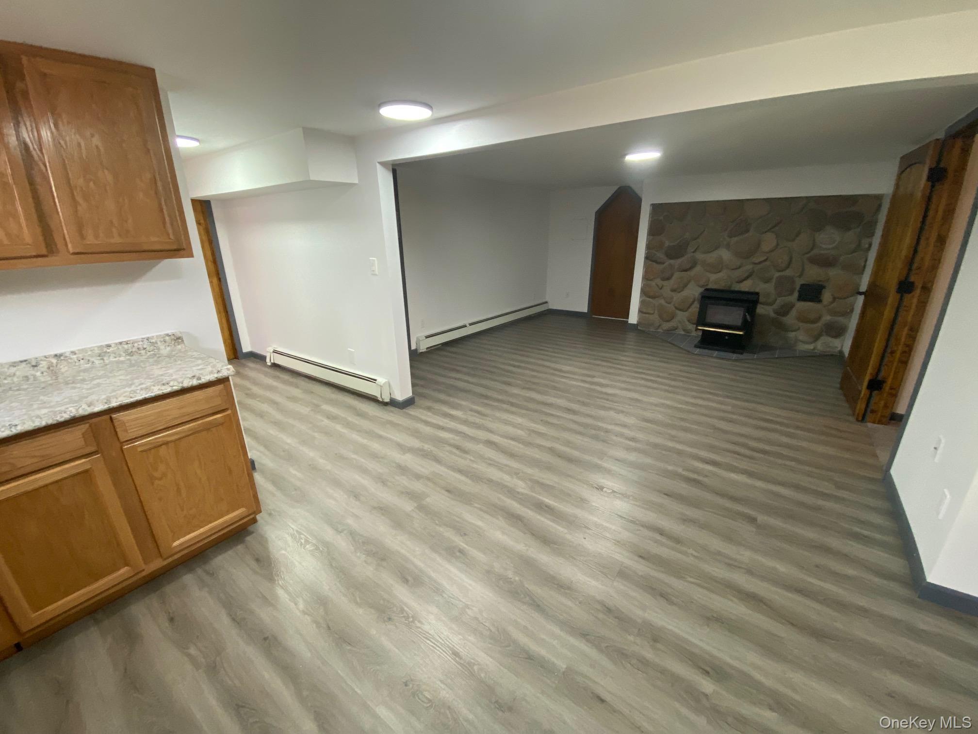 315 Upper Road, Unit LOWR Middletown, NY 10940 - Photo 4 of 9 Unfurnished living room featuring a wood stove, light hardwood / wood-style floors, and a baseboard heating unit