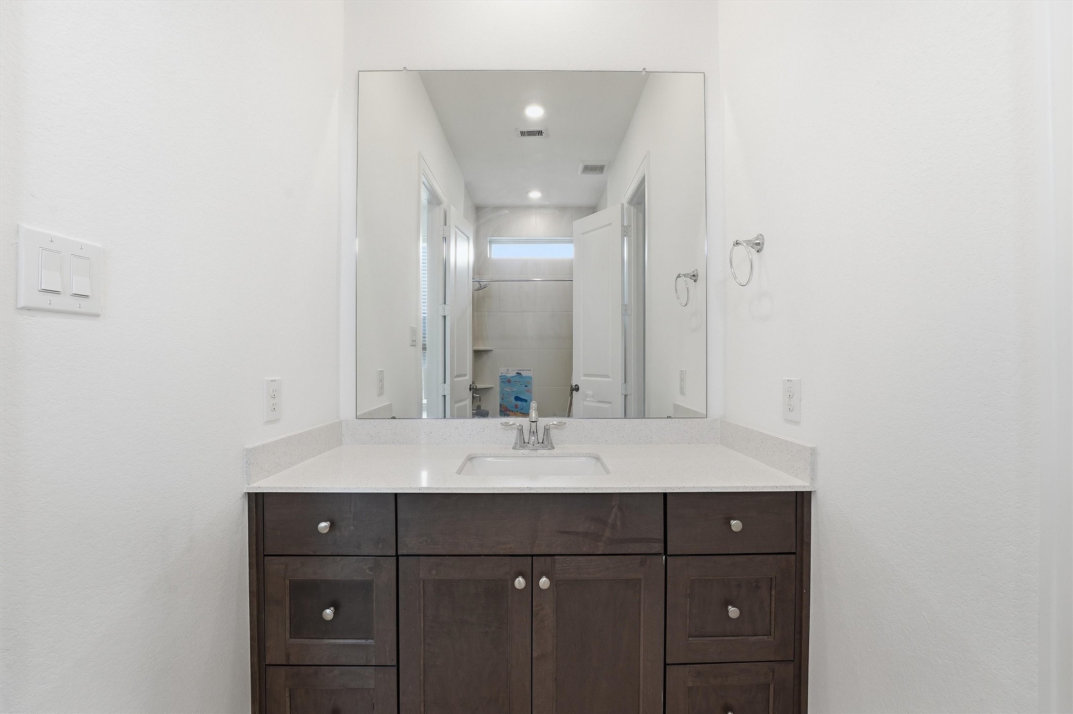 6071 Windward Falls Way Porter, TX 77365 - Photo 6 of 33 This photo features a modern bathroom vanity with a sleek countertop, a large mirror, and ample storage in dark wood cabinets. The space is bright and clean, ideal for a contemporary home.