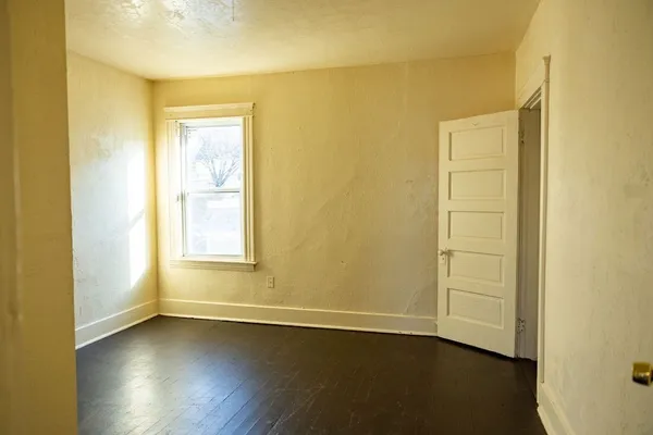 a view of an empty room with wooden floor and a window