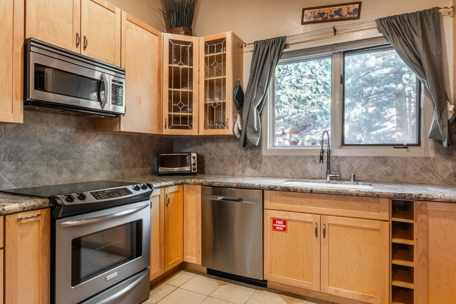 2112 Meridian Boulevard, Unit 7 Mammoth Lakes, CA 93546 - Photo 8 of 33 Kitchen with appliances with stainless steel finishes, glass insert cabinets, light brown cabinets, and backsplash