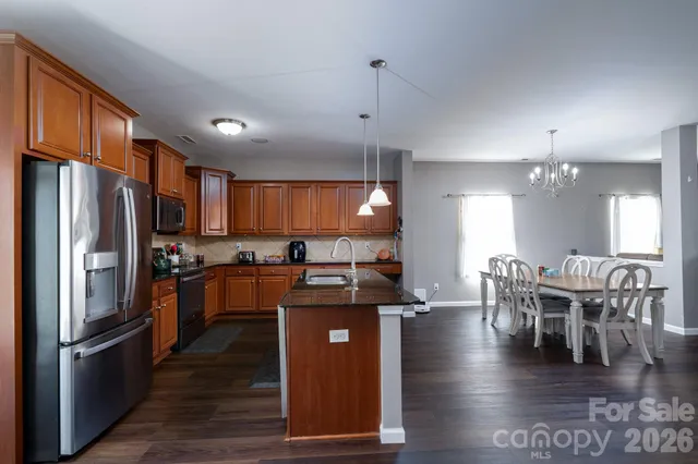 a kitchen with stainless steel appliances granite countertop a refrigerator a stove top oven a dining table and chairs with wooden floor