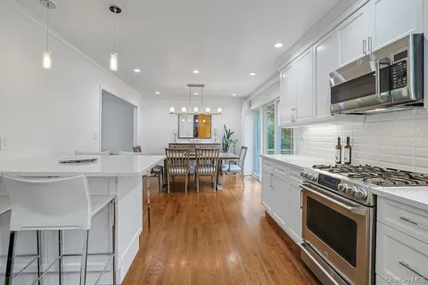 a kitchen with stainless steel appliances a stove a sink a microwave a stove and white cabinets with wooden floor
