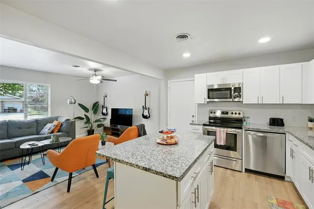 a kitchen with stainless steel appliances granite countertop a stove top oven a sink dishwasher a dining table and chairs with wooden floor