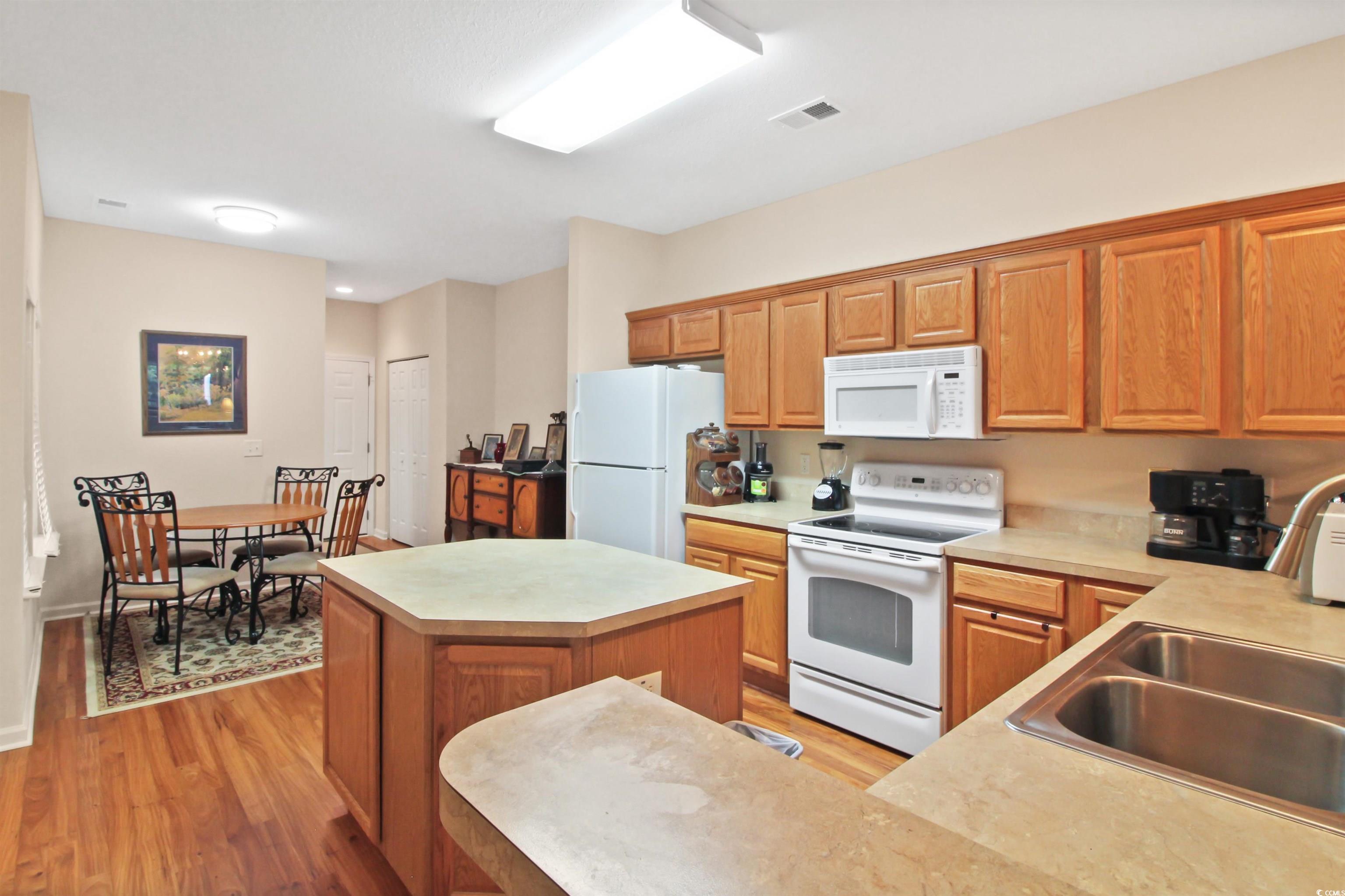 Kitchen with white appliances, a center island, light wood-style floors, light countertops, and brown cabinetry
