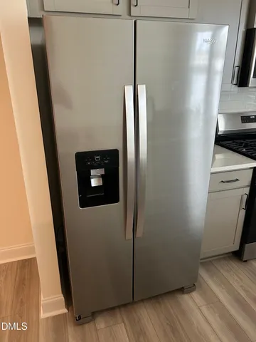 a view of a refrigerator in kitchen and an empty room with wooden floor