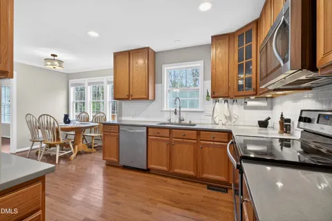 a kitchen with stainless steel appliances granite countertop wooden cabinets a sink a stove a dining table and chairs
