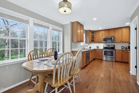 a kitchen with granite countertop a stove a sink a refrigerator dining table chairs and a large window