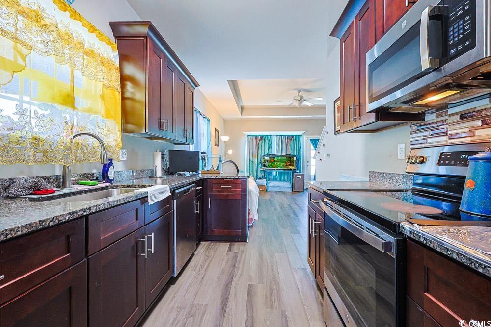 724 Hobonny Loop Longs, SC 29568 - Photo 8 of 40 Kitchen with appliances with stainless steel finishes, light stone countertops, light wood-type flooring, a raised ceiling, and a ceiling fan