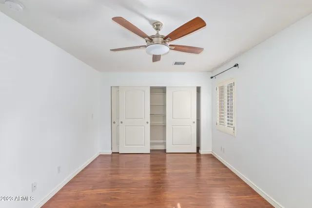 an empty room with wooden floor ceiling fan and windows