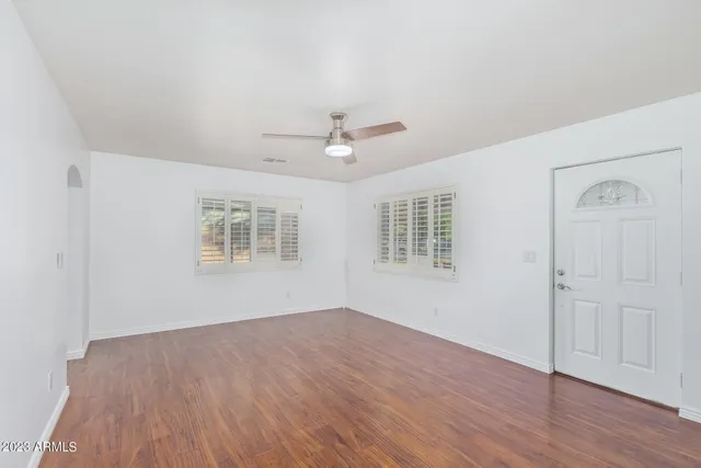 an empty room with wooden floor ceiling fan and windows