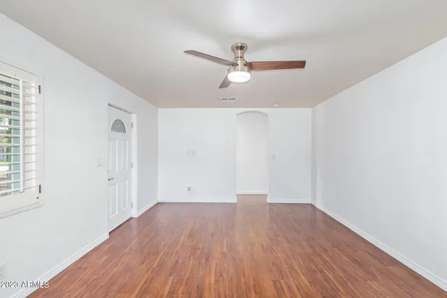 an empty room with wooden floor ceiling fan and windows