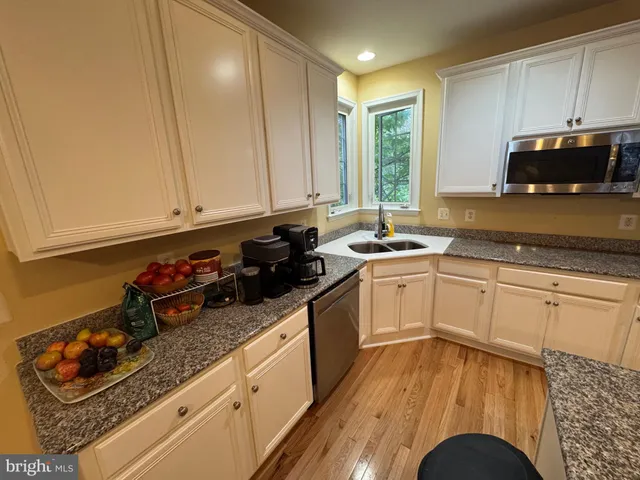 a kitchen with granite countertop a stove a sink dishwasher and white cabinets with wooden floor