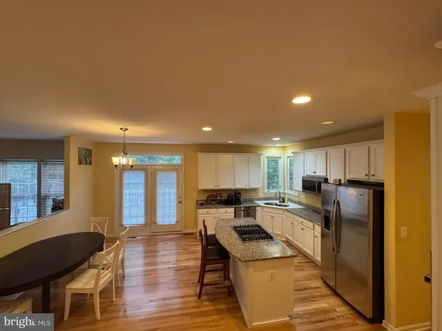 a kitchen with granite countertop a refrigerator a stove a sink a dining table and chairs with wooden floor